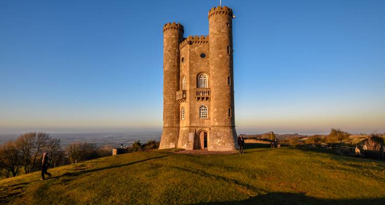 Historic tower on a grassy hill with people exploring.