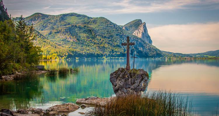 Lac serein avec un monument en forme de croix et un arrière-plan montagneux.