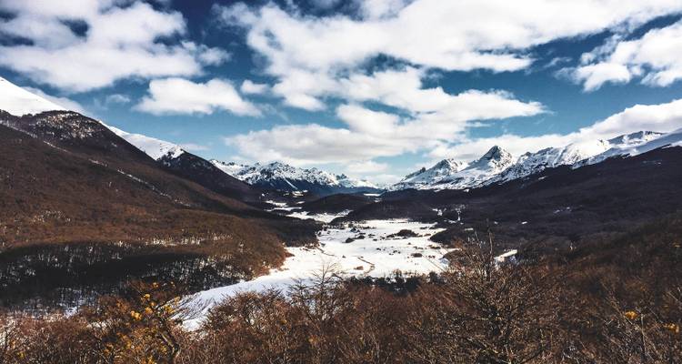 Vallée de montagne enneigée avec forêt et ciel.