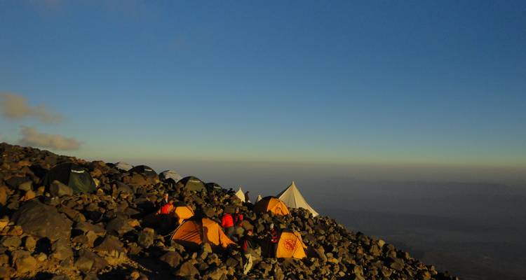 Campsite with tents on a rocky mountain slope at sunrise.