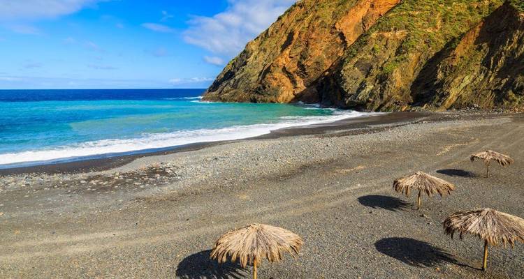 Plage avec parasols en paille et falaises rocheuses.