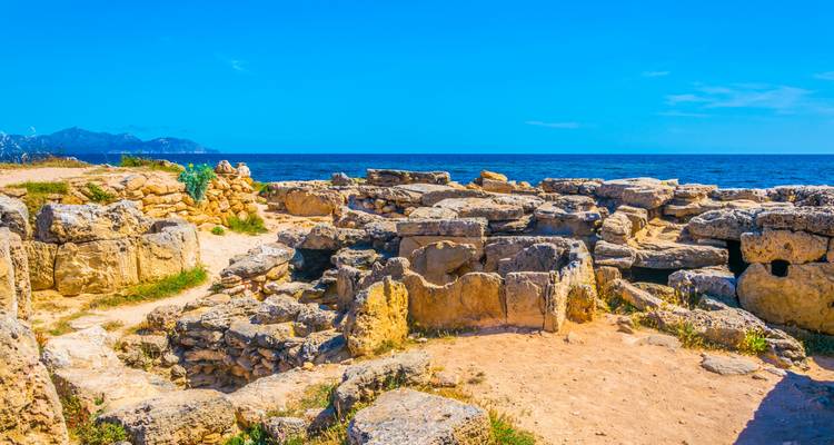 Ruines anciennes le long d'une côte rocheuse sous un ciel bleu dégagé.