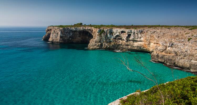 Falaises escarpées et mer turquoise cristalline sous un ciel lumineux.