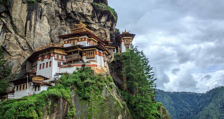 El Monasterio del Nido del Tigre encaramado dramáticamente en un acantilado rodeado de montañas boscosas.