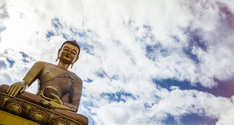 Enorme estatua de Buda de bronce sentado elevándose contra un cielo dramático lleno de nubes cerca de Thimphu.