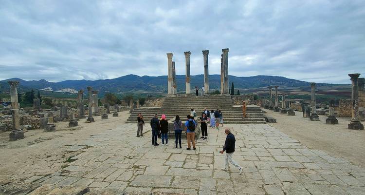 Touristen erkunden antike Ruinen mit Bergen im Hintergrund.