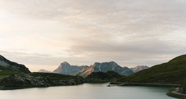 Ruhiger See vor einer bergigen Landschaft bei Sonnenuntergang