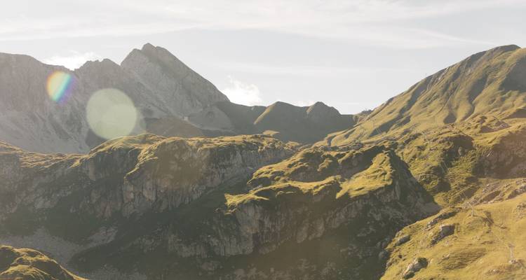 Berglandschaft mit grünen Hängen und Sonnenlichtreflexen.