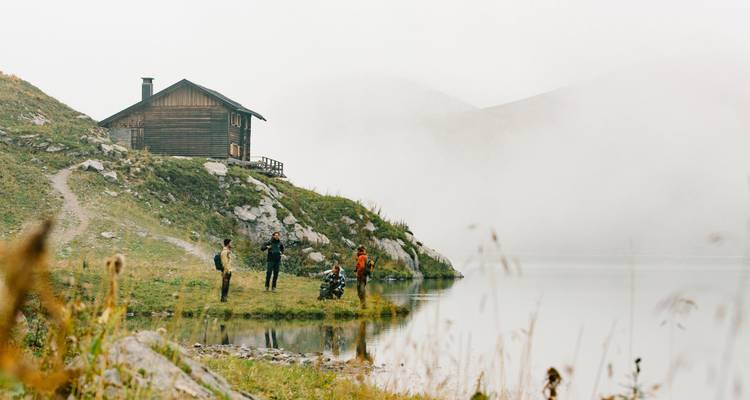 Gruppe von Menschen an einem See und einer Hütte im Nebel.