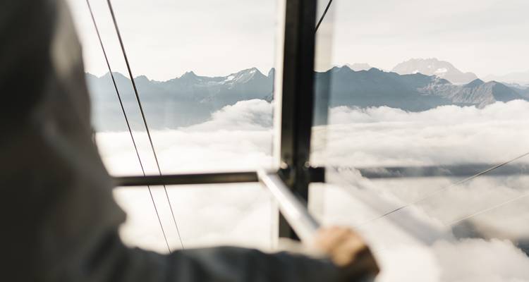 Blick aus einer Seilbahn über Wolken und Berggipfel.
