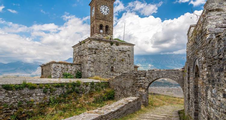 Torre del reloj histórica y sendero de piedra con vistas a las montañas.