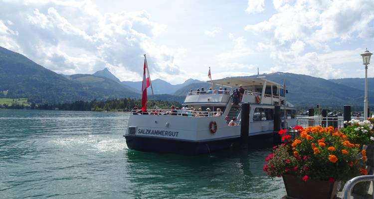 Een veerboot genaamd 'Salzkammergut' aangemeerd aan een pier op een schilderachtig meer met bergen op de achtergrond.