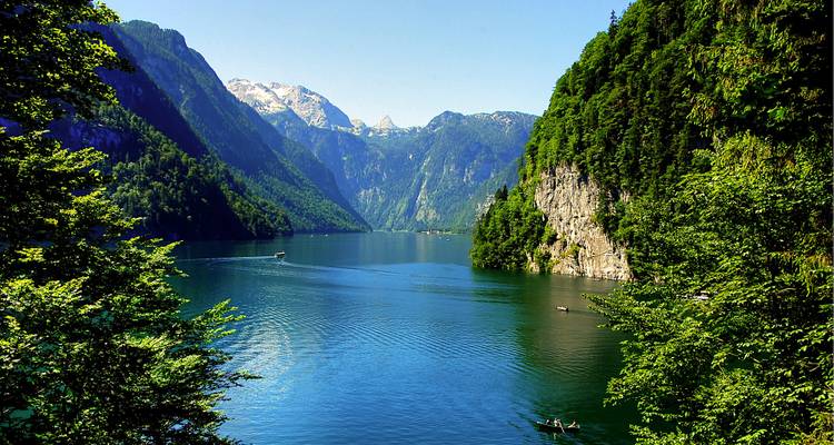 Scenic view of a lake surrounded by mountains with a boat and a sunny sky.