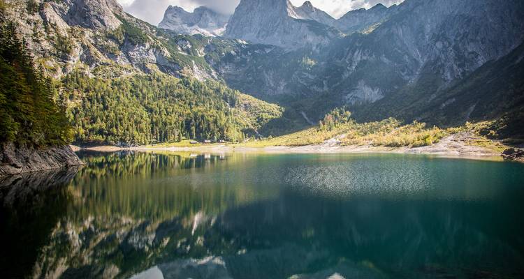 Bergsee umgeben von Wäldern und Gipfeln.