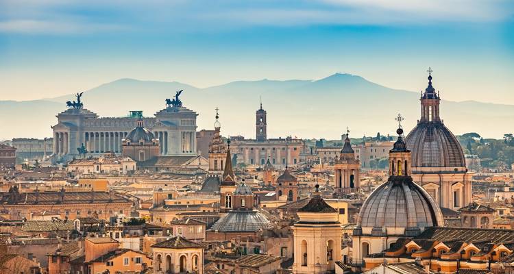 Vista panorámica del horizonte de Roma con edificios históricos y montañas al fondo.