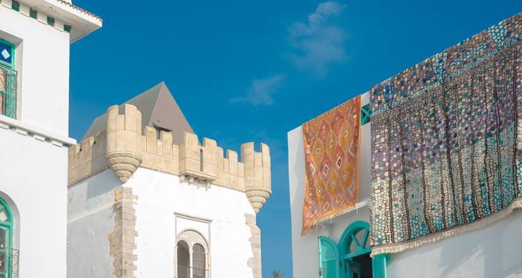 Wit gebouw met decoratieve gevel en kleurrijke textiel die buiten hangt.