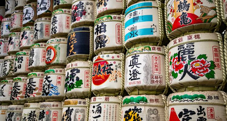 Gestapelte dekorative Sake-Fässer mit bunten Kanji-Designs an einem Schrein