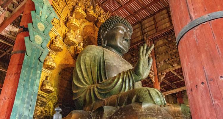 Massive sitzende Bronzebuddha-Statue in einer Holzhalle mit kunstvollen Schnitzereien