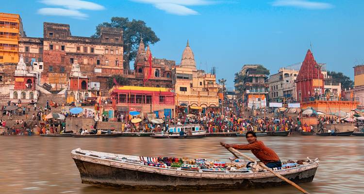 Belebte Ghats von Varanasi mit bunten Gebäuden und einem einsamen Bootshändler auf dem Ganges