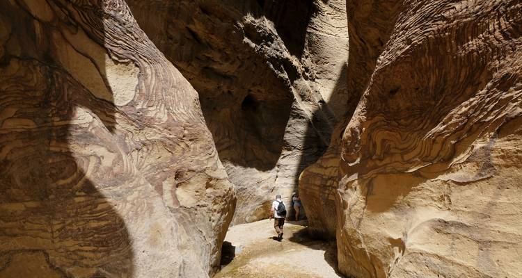 Wanderer gehen durch schmale, geschwungene Sandsteinschluchtenwände, die mit farbigen Schichtungen geätzt sind.