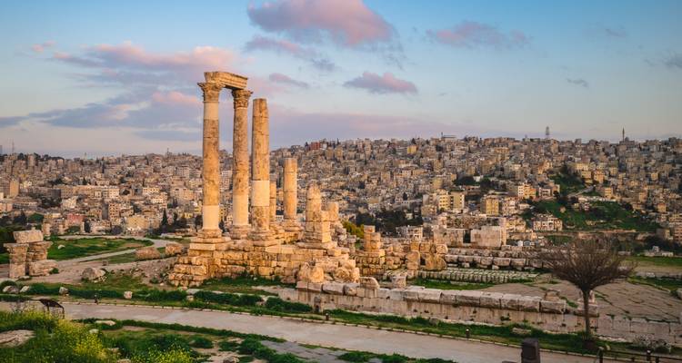 Antike römische Säulen des Herkules-Tempels überblicken die weitläufige Stadt Amman unter einem warmen Sonnenuntergangshimmel.