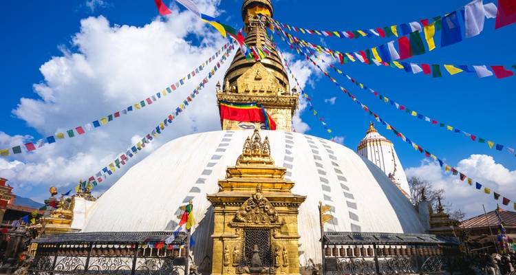 White Swayambhunath stupa crowned with golden spire and vibrant prayer flags against blue sky.
