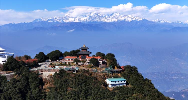 Hilltop temple complex of Nagarkot framed by forested ridge with snowy Himalaya behind.