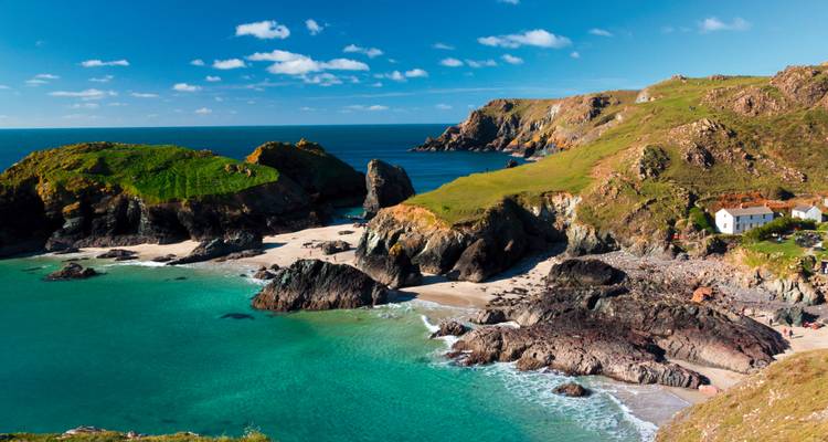 A pristine sandy cove with emerald water and rugged headlands under a bright blue sky on the Cornish coast.