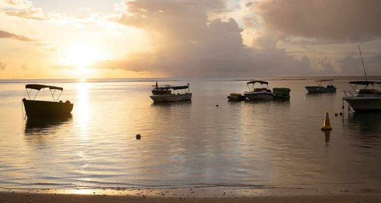 Scène de plage sereine avec des bateaux au coucher du soleil.