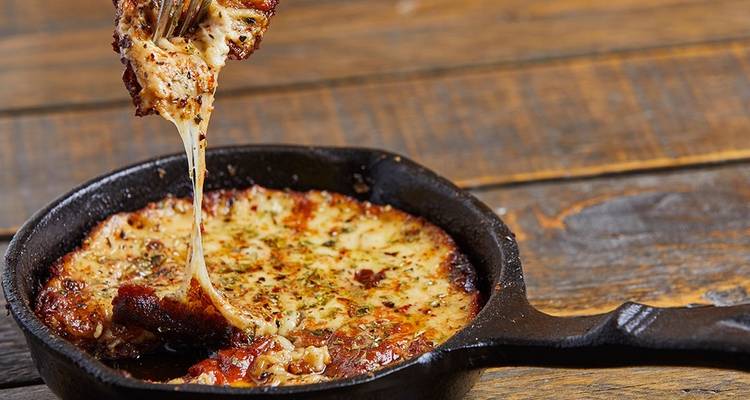 Gros plan sur du fromage grésillant dans une poêle en fonte sur une table en bois