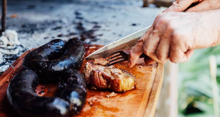 Personne découpant des saucisses grillées et de la viande sur une planche en bois