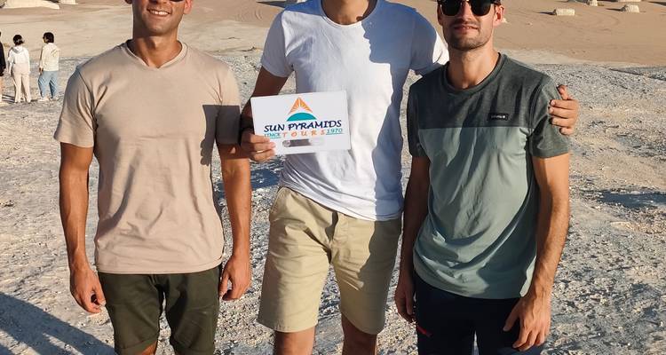 Three people posing with a tour sign in a desert.