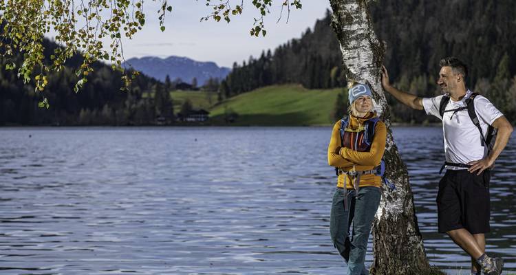 Wandelend stel dat rust tegen een berken naast een rustig meer met glooiende heuvels en verre pieken