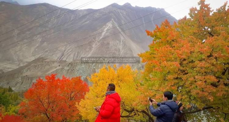 Zwei Personen in einem Park mit bunten Herbstblättern und einer Bergkulisse im Hintergrund.