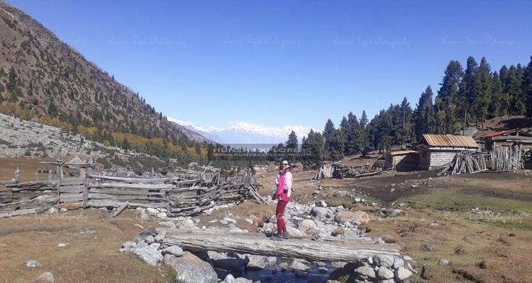 Person, die auf einer rustikalen Holzbrücke in einer ländlichen Landschaft mit Bergen steht.