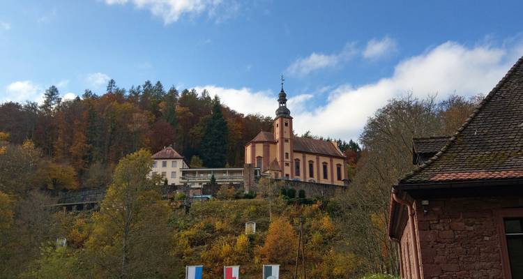 Malerische Bergkirchenkirche erhebt sich über bunten Herbstwald unter blauem Himmel.