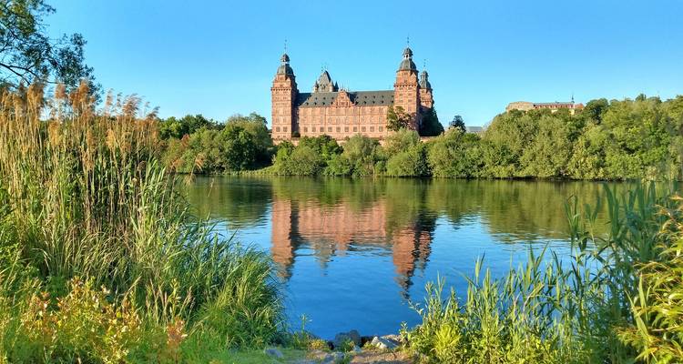 Historic red-sandstone castle reflected perfectly in a calm river on a clear morning.