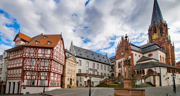 Historischer Marktplatz mit Fachwerkhäusern und prunkvoller Kirche unter dramatischen Wolken.