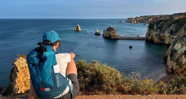 Rucksacktourist sitzt am Klippenrand und bewundert Felsformationen und blaues Meer an der Ponta da Piedade