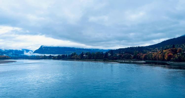 A serene lake scene with forested hills and cloudy skies.