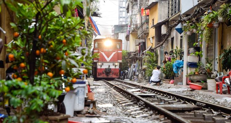 Train passant par une rue étroite bordée de bâtiments résidentiels.