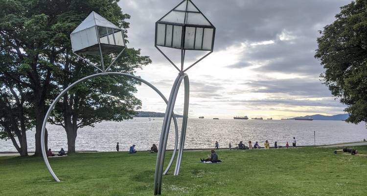 Grande installation d'art métallique sur le front de mer avec des gens sur l'herbe.