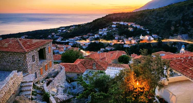 A scenic view of a coastal village at sunset, with lights illuminating the houses.