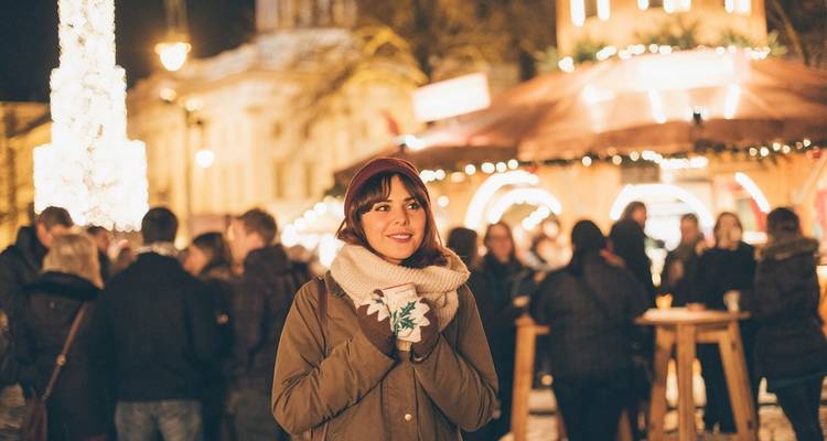 Mujer disfrutando de un mercado navideño al aire libre por la noche.