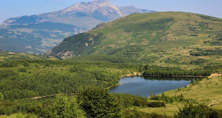 Malerische Aussicht auf einen See, umgeben von bewaldeten Hügeln und Bergen.