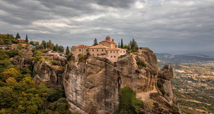 Monastère au sommet de falaises avec des nuages dramatiques.