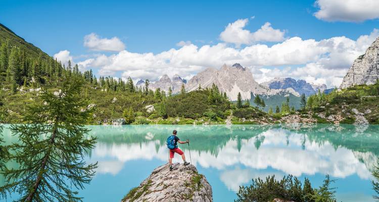 Hiker standing in front of a stunning turquoise lake with mountains in the background.