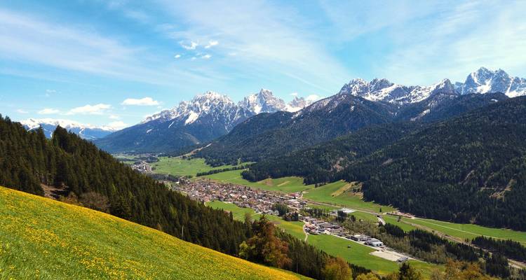 Village de montagne niché dans une vallée avec des sommets enneigés en arrière-plan.