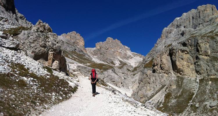 Randonneur avec sac à dos marchant le long d'un sentier de montagne accidenté bordé par de spectaculaires falaises des Dolomites.