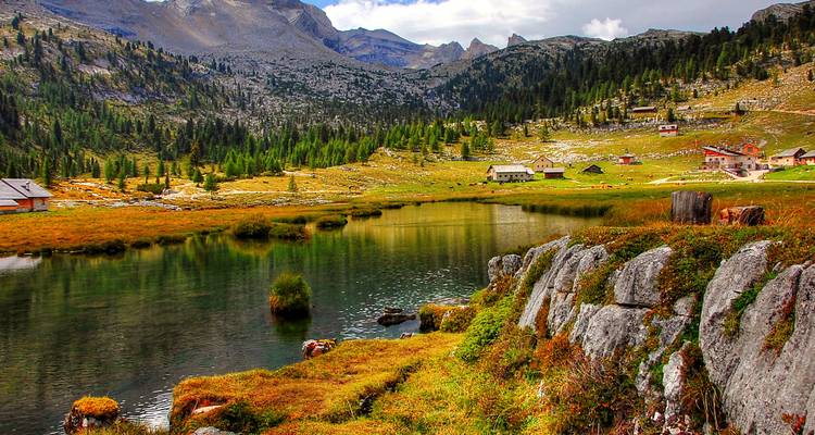 Lac alpin paisible entouré de prairies aux teintes automnales et dominé par des pics rocheux.